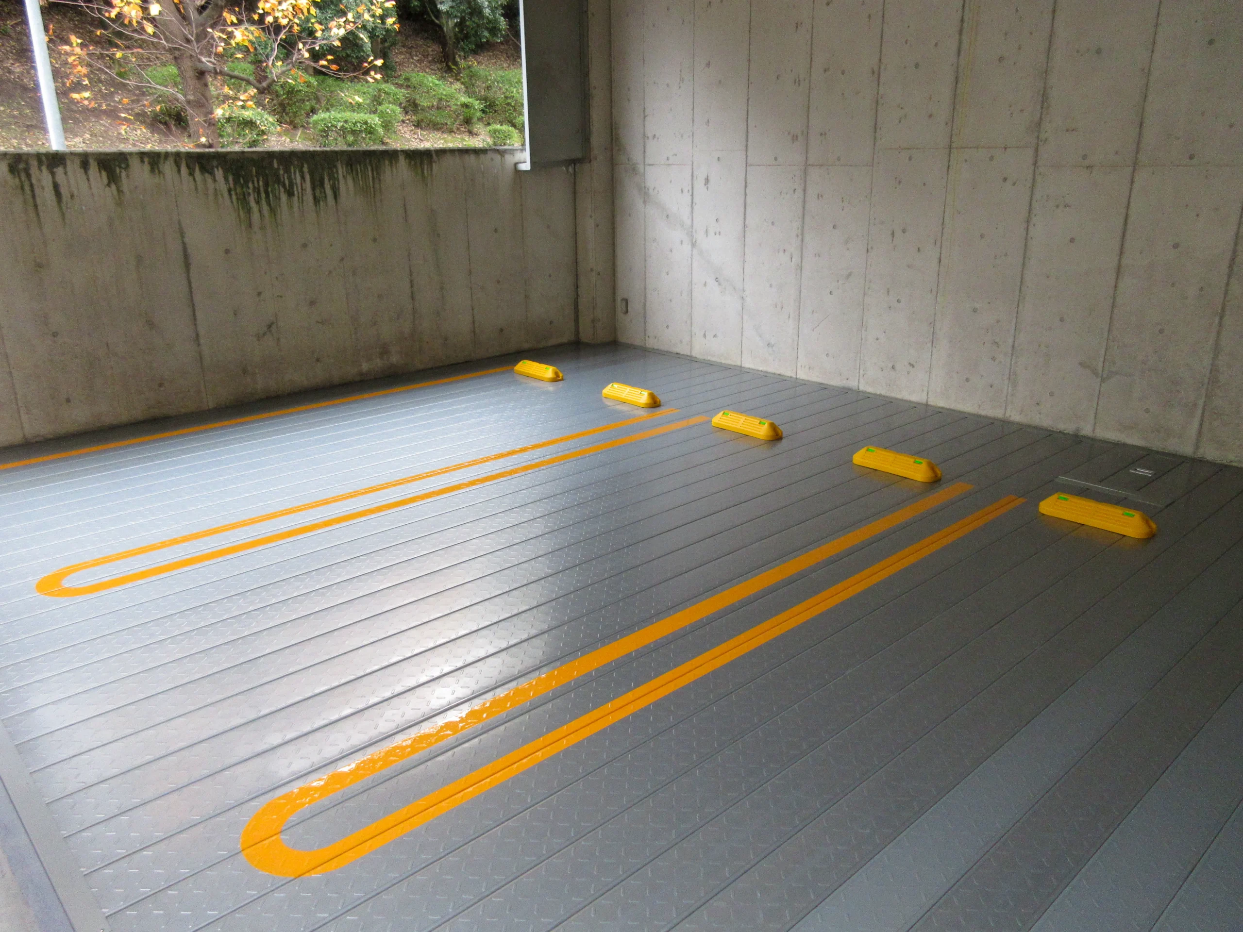 グレーの床面塗装を施し、黄色のＵ字型のラインと車止めを設置した屋内駐車場の施工後写真
