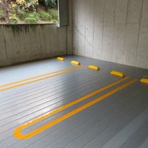 グレーの床面塗装を施し、黄色のＵ字型のラインと車止めを設置した屋内駐車場の施工後写真